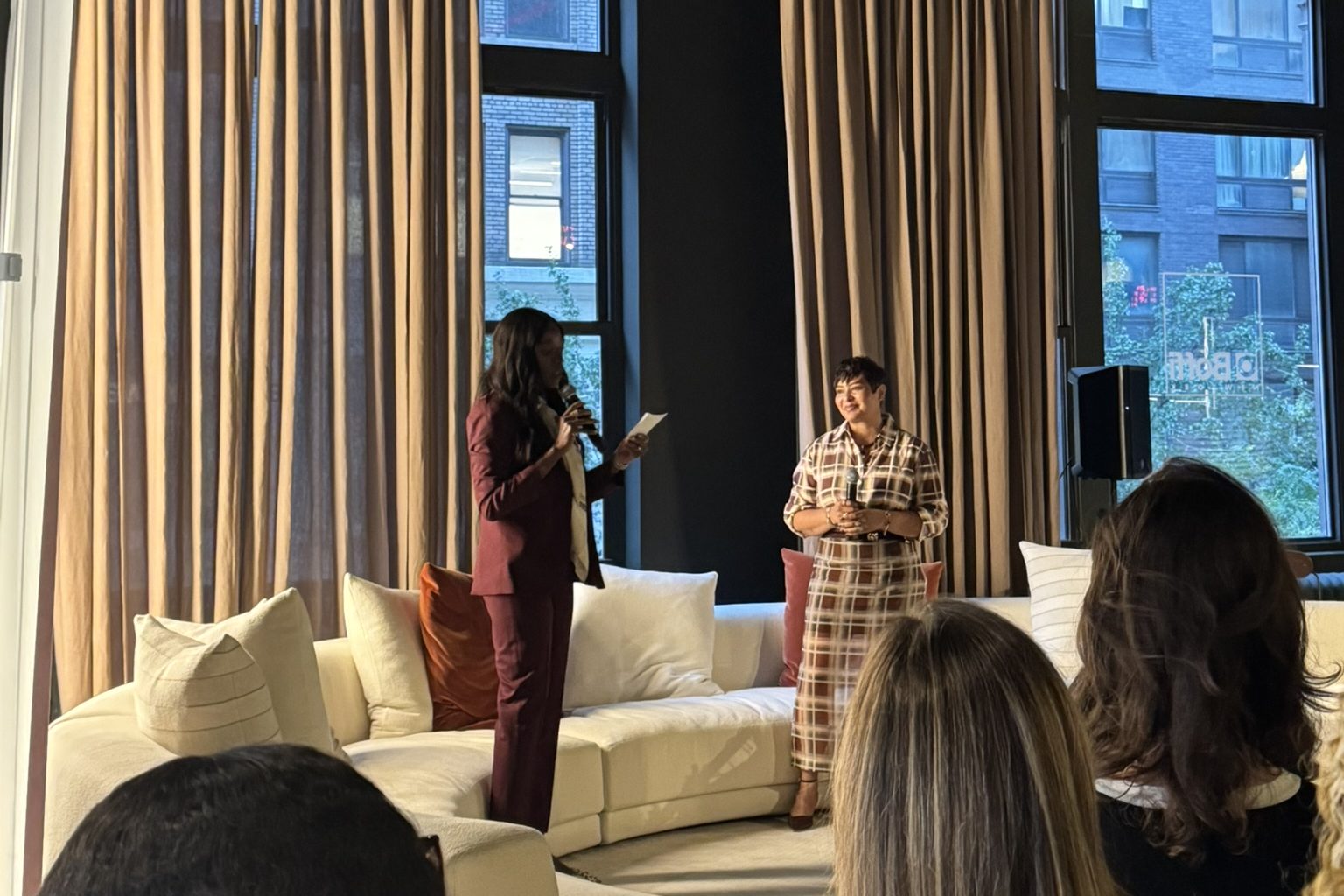 Stephanie holding a microphone beside the host at a fireside chat in a loft event space