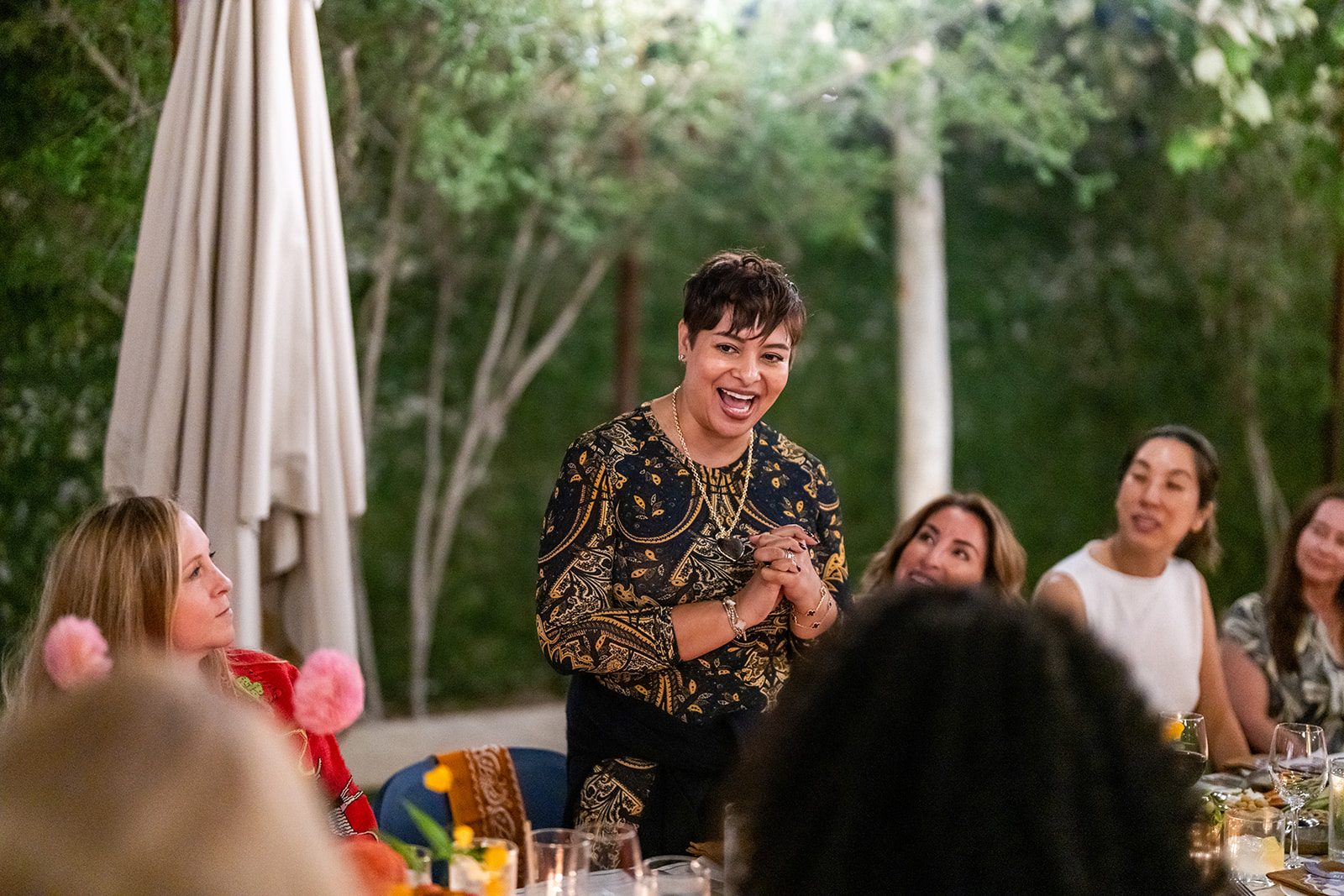 Stephanie speaking to guests at a candlelit outdoor dinner table
